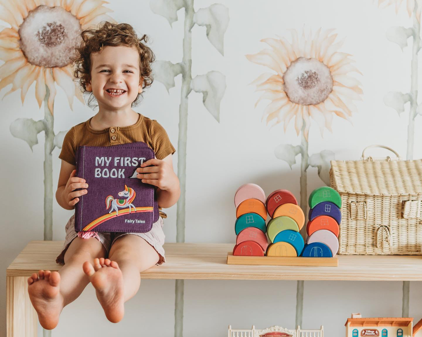 My First Book held by a smiling boy sitting on a shelf