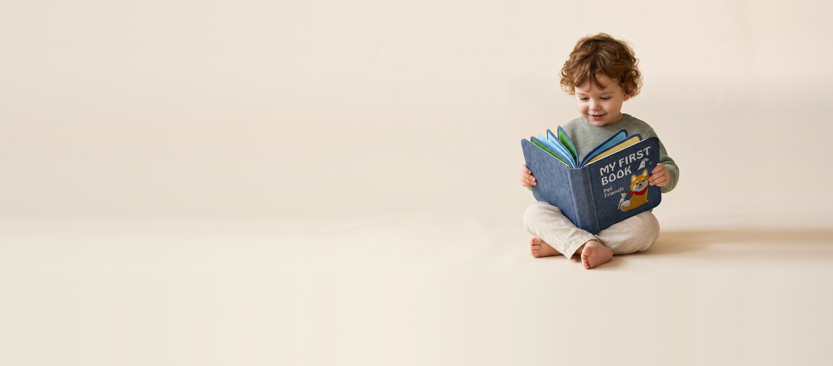 Kleinkind sitzt im Schneidersitz und liest lächelnd im My First Book Pet Friends Quiet Book