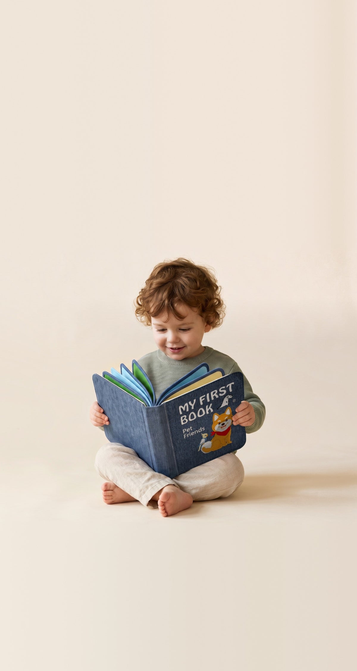 Kleinkind sitzt im Schneidersitz und liest lächelnd im My First Book Pet Friends Quiet Book